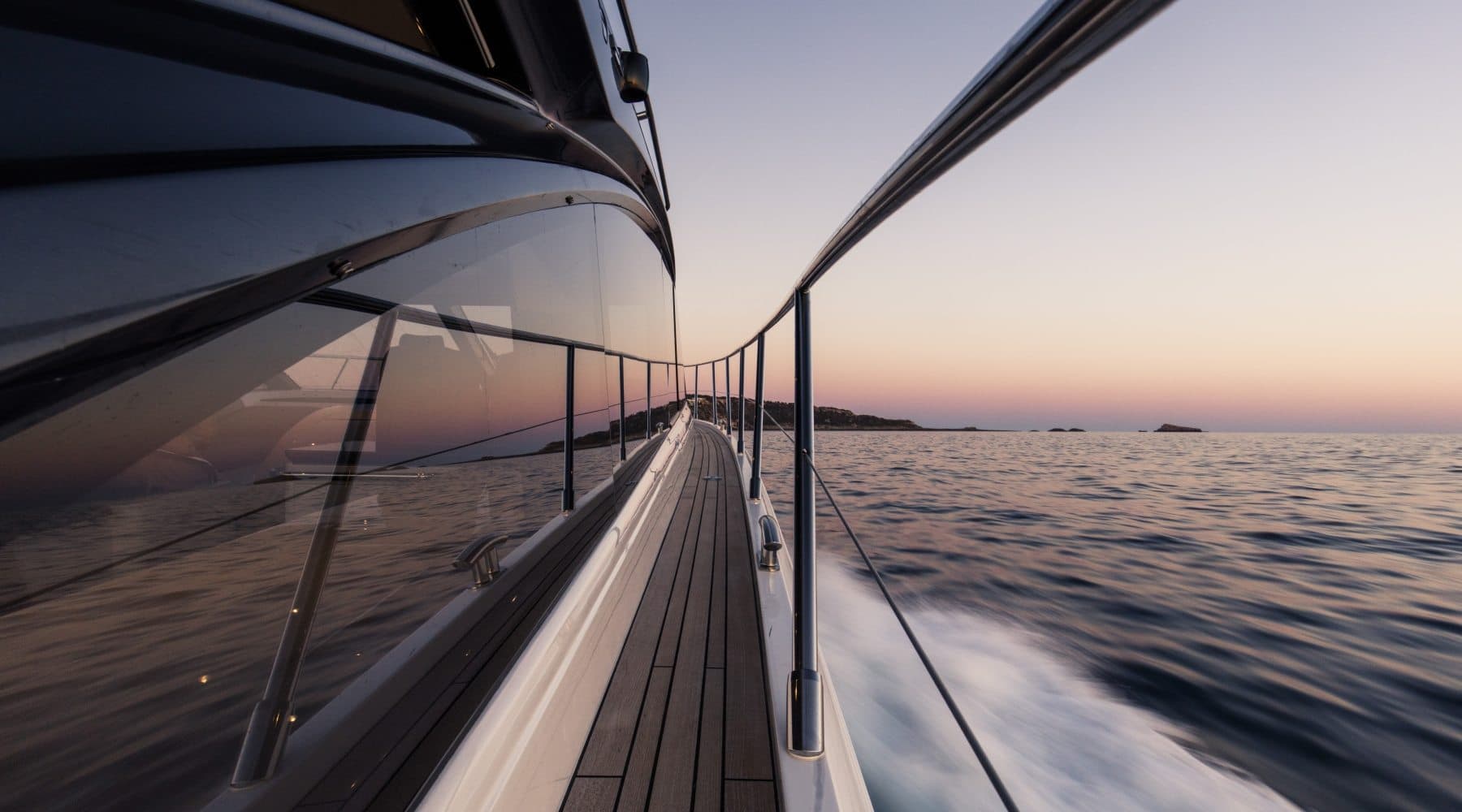 Teak side deck looking forward underway at sea with sunset and wake